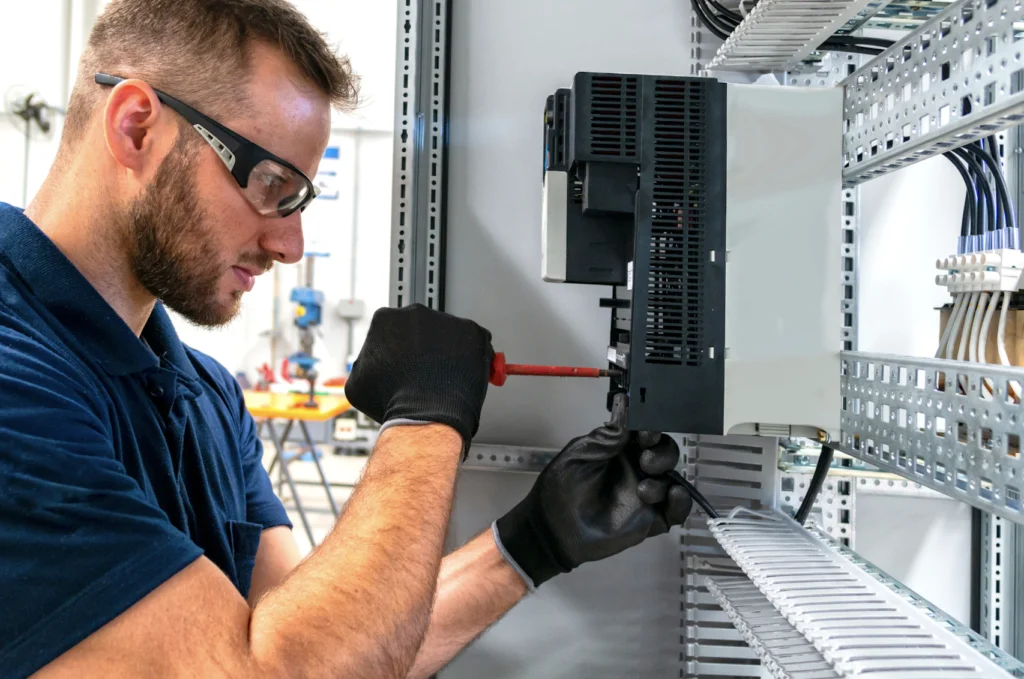 Male electrician wearing safety equipment, working on some equipment in an industrial property as an electrical contractor.