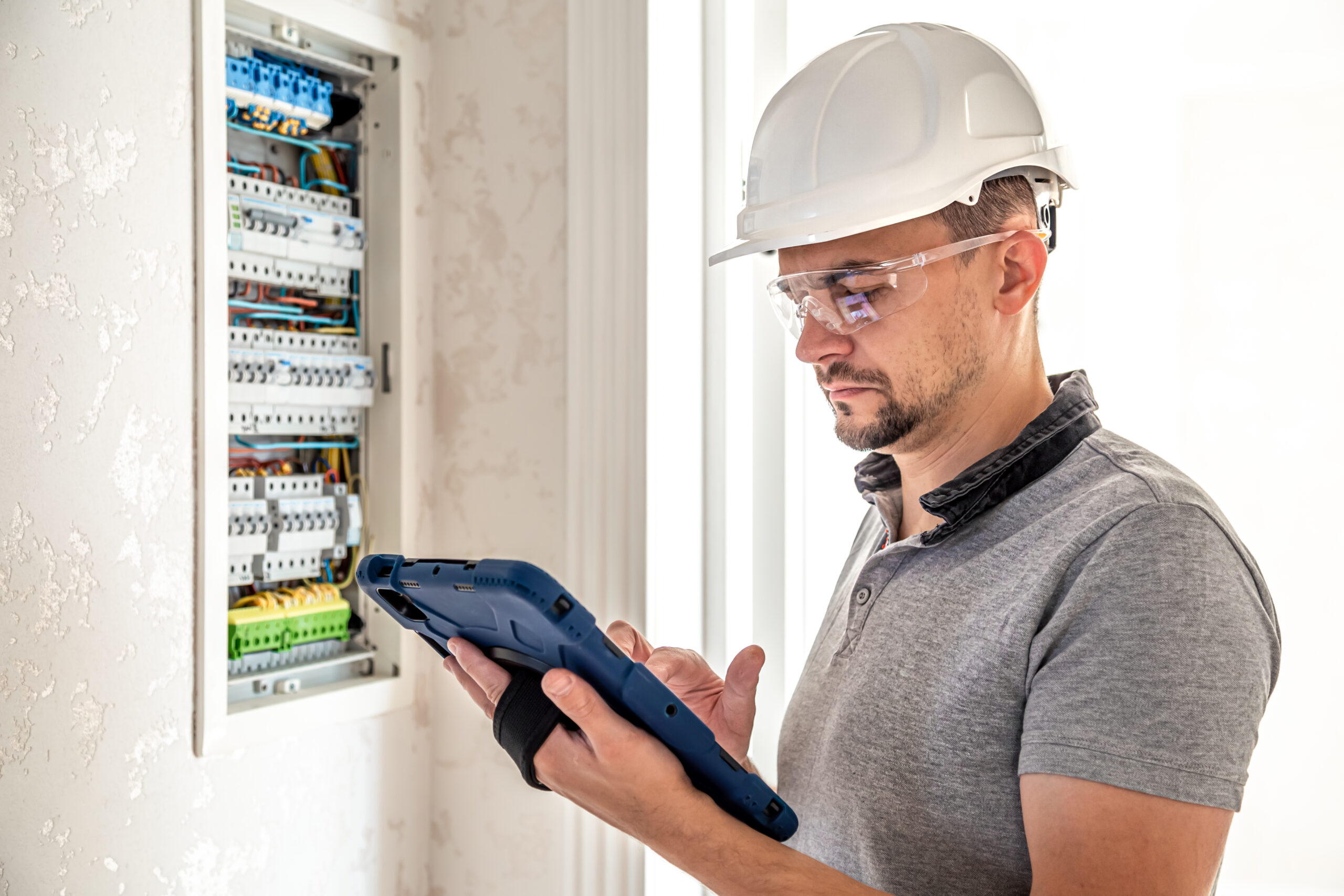 Electrician using a tablet to inspect a distribution board during a commercial fit-out
